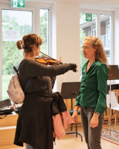 Julia von Niswandt steht vor einer Besucherin, welche auf einer Geige spielt.